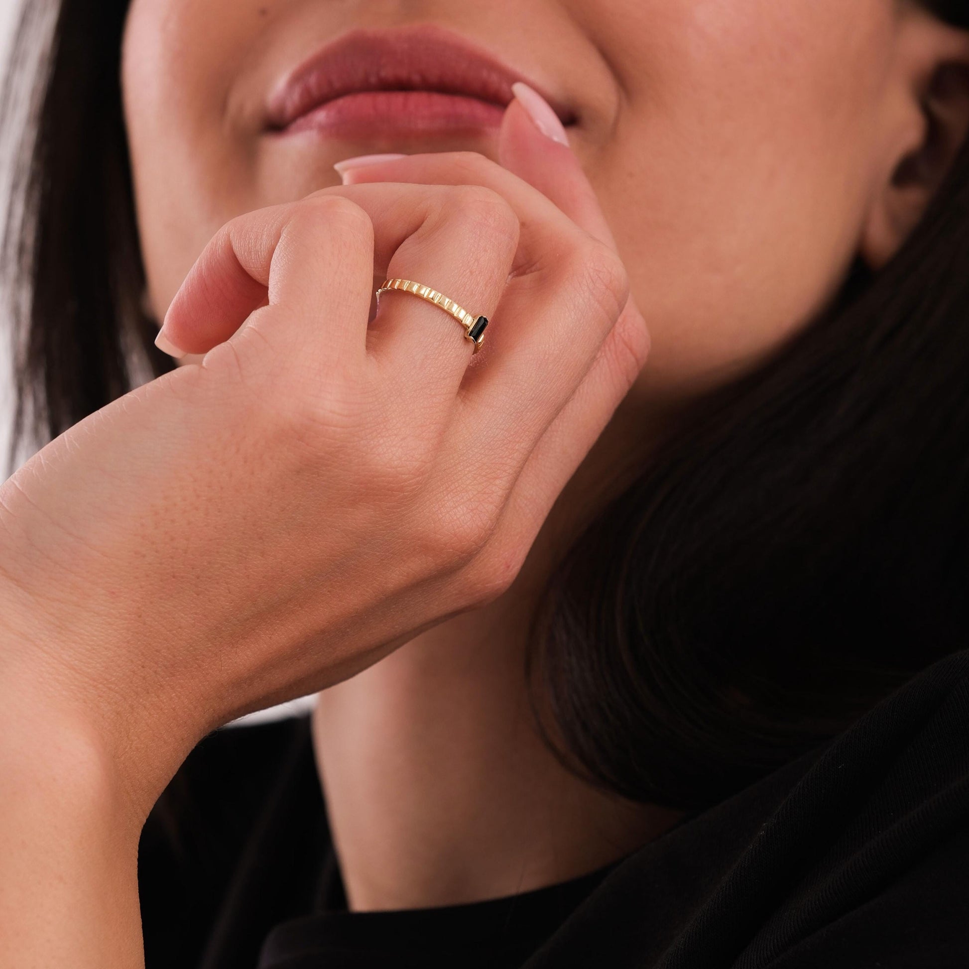 Close-up of a 14K solid gold black onyx ring on a bent finger, with the rectangular onyx gemstone angled outward.