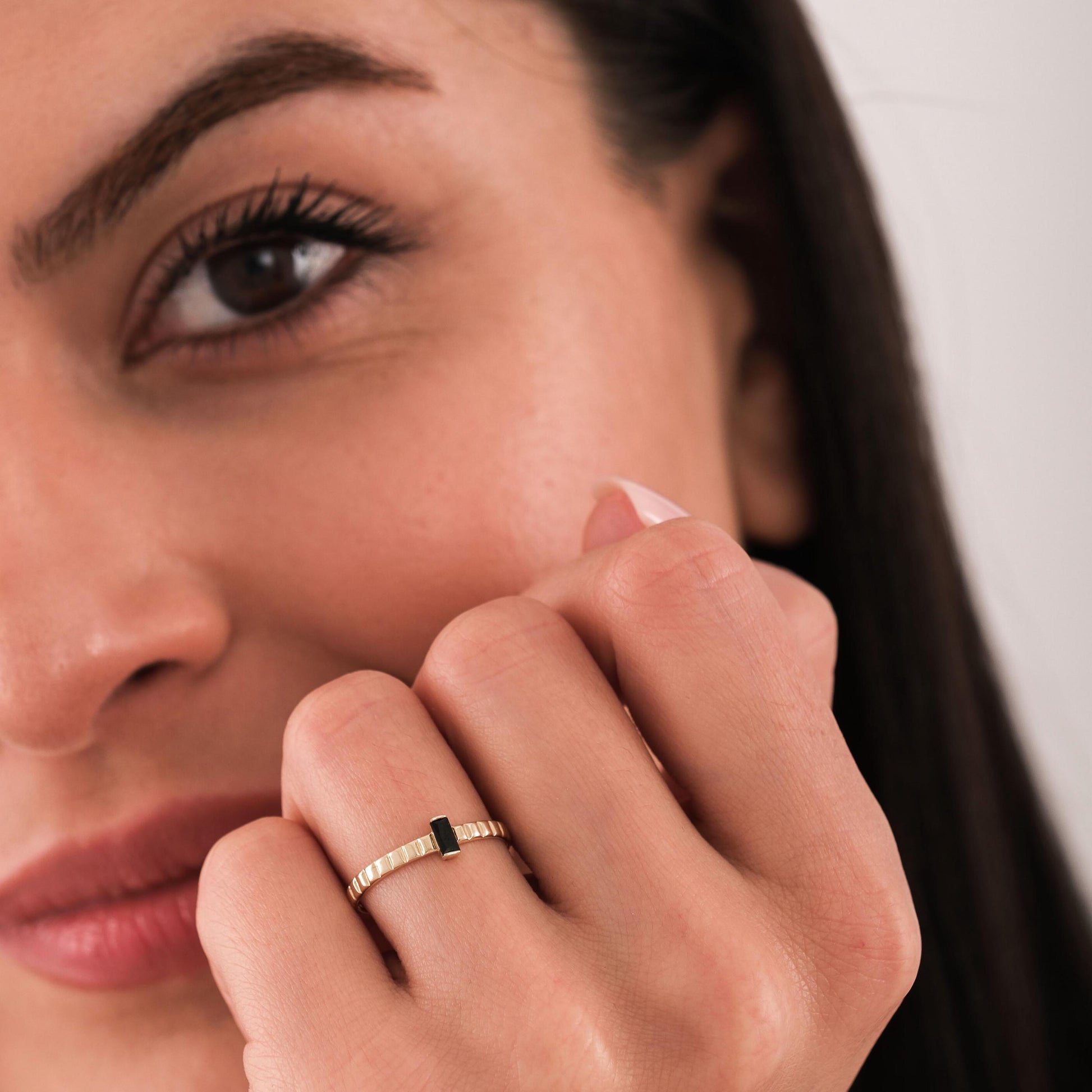 Close-up of a woman's hand showing a 14K solid gold black onyx ring with a rectangular stone on a textured band.