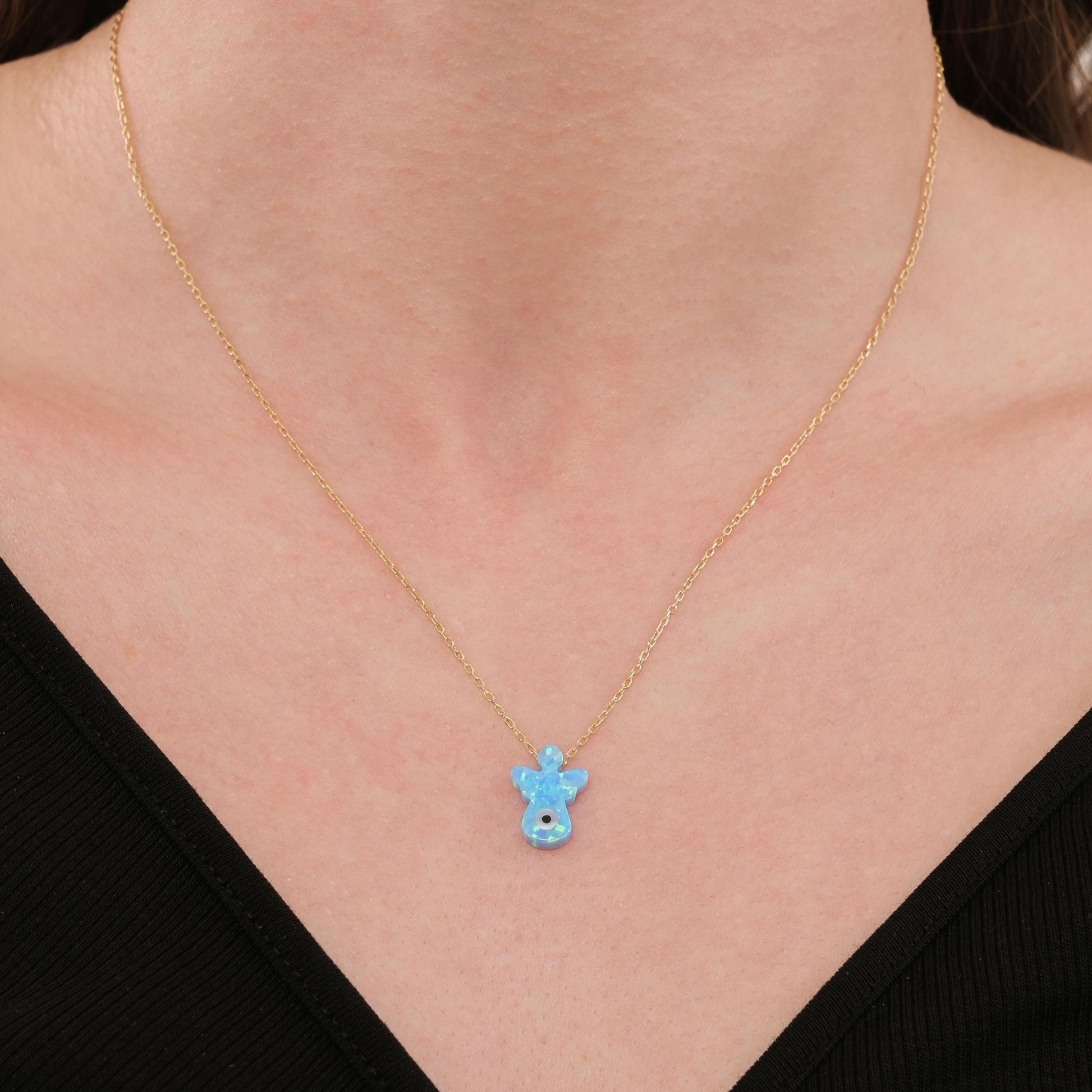Close-up of the 14K solid gold opal angel necklace styled with a black top, highlighting the charm’s vivid blue hue.