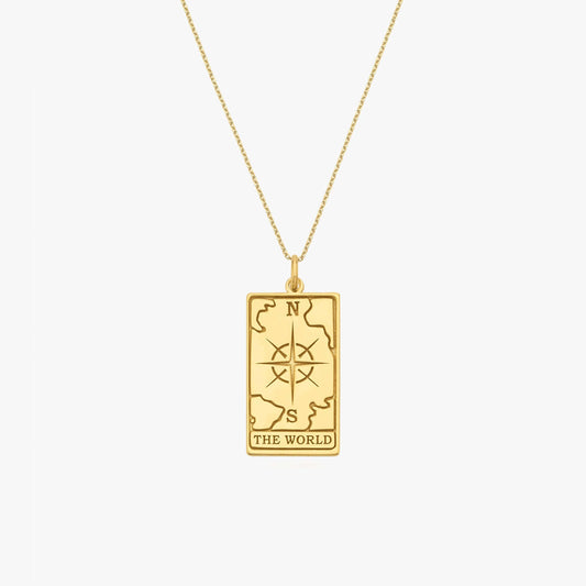 Gold necklace with rectangular pendant featuring compass design and "The World" engraving, symbolizing global journey.