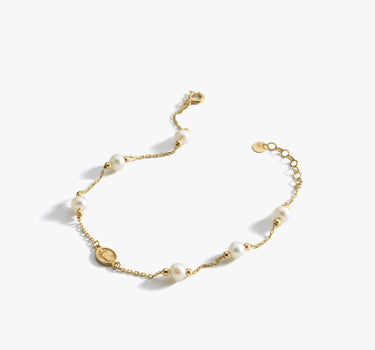 The Mionza Miraculous Medal Bracelet with Real Pearl is a delicate 14K solid gold chain bracelet adorned with white pearls and small gold beads. It features an adjustable clasp and a tiny coin charm near the closure. This elegant and minimalist design is perfect for various occasions.