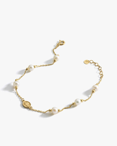 The Mionza Miraculous Medal Bracelet with Real Pearl is a delicate 14K solid gold chain bracelet adorned with white pearls and small gold beads. It features an adjustable clasp and a tiny coin charm near the closure. This elegant and minimalist design is perfect for various occasions.