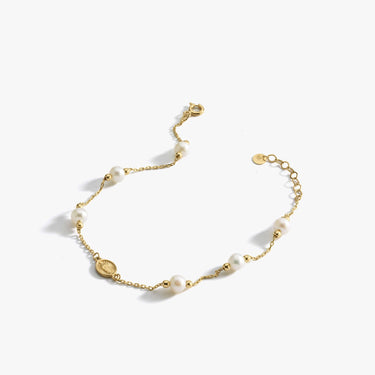 The Mionza Miraculous Medal Bracelet with Real Pearl is a delicate 14K solid gold chain bracelet adorned with white pearls and small gold beads. It features an adjustable clasp and a tiny coin charm near the closure. This elegant and minimalist design is perfect for various occasions.