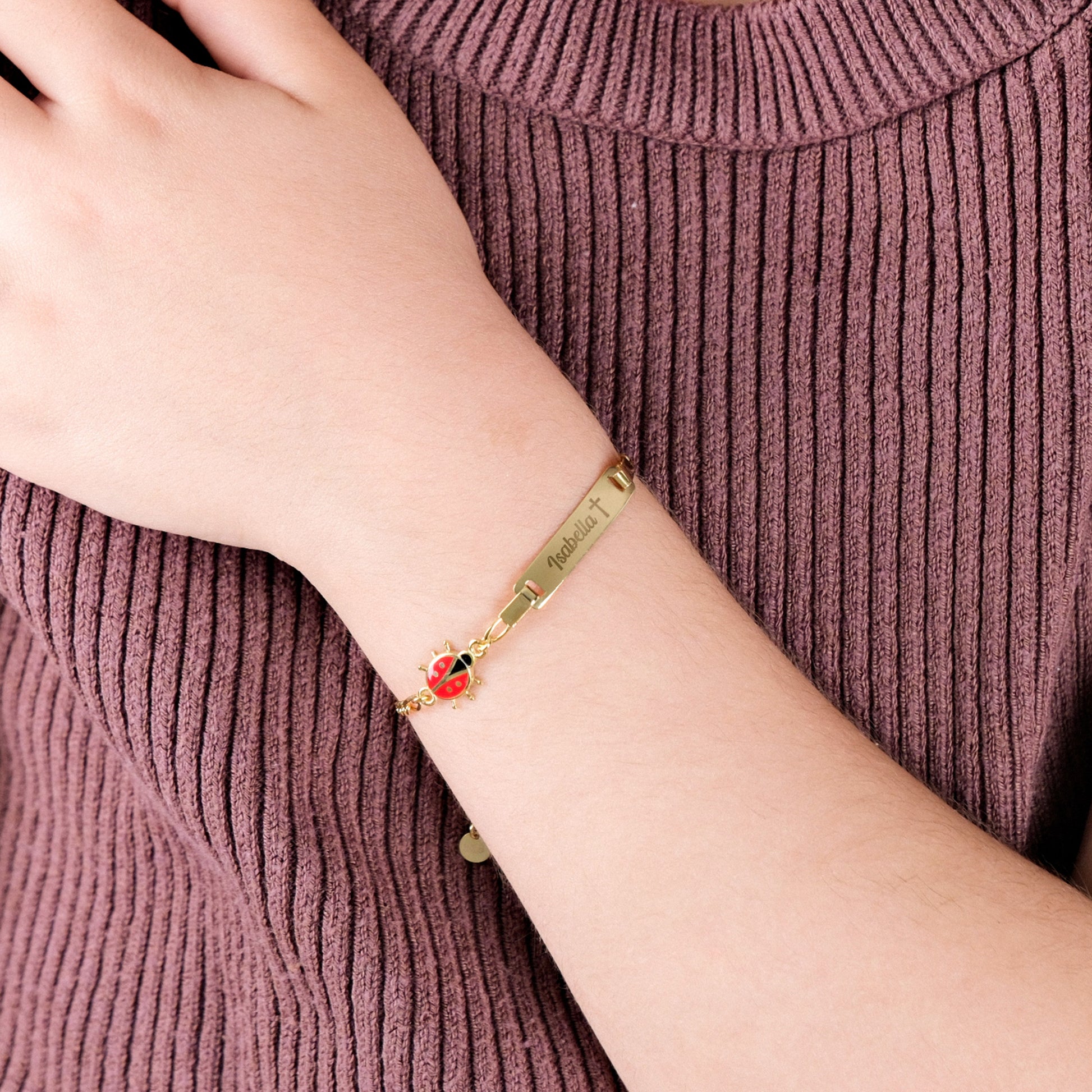 Gold bracelet for baby with a ladybug charm on a wrist against a ribbed fabric background