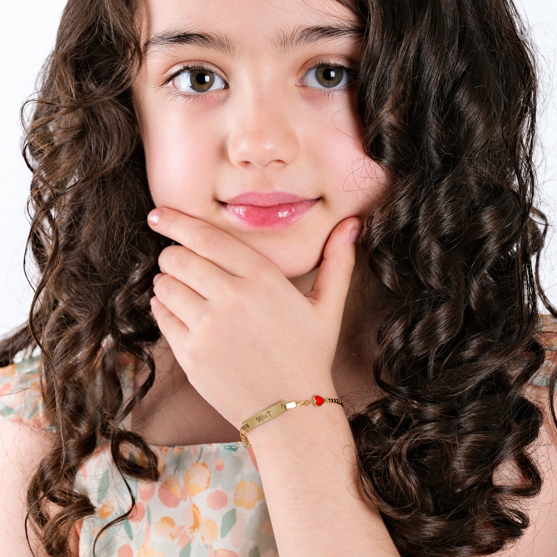 Young girl with curly hair and a floral dress, wearing a bracelet.