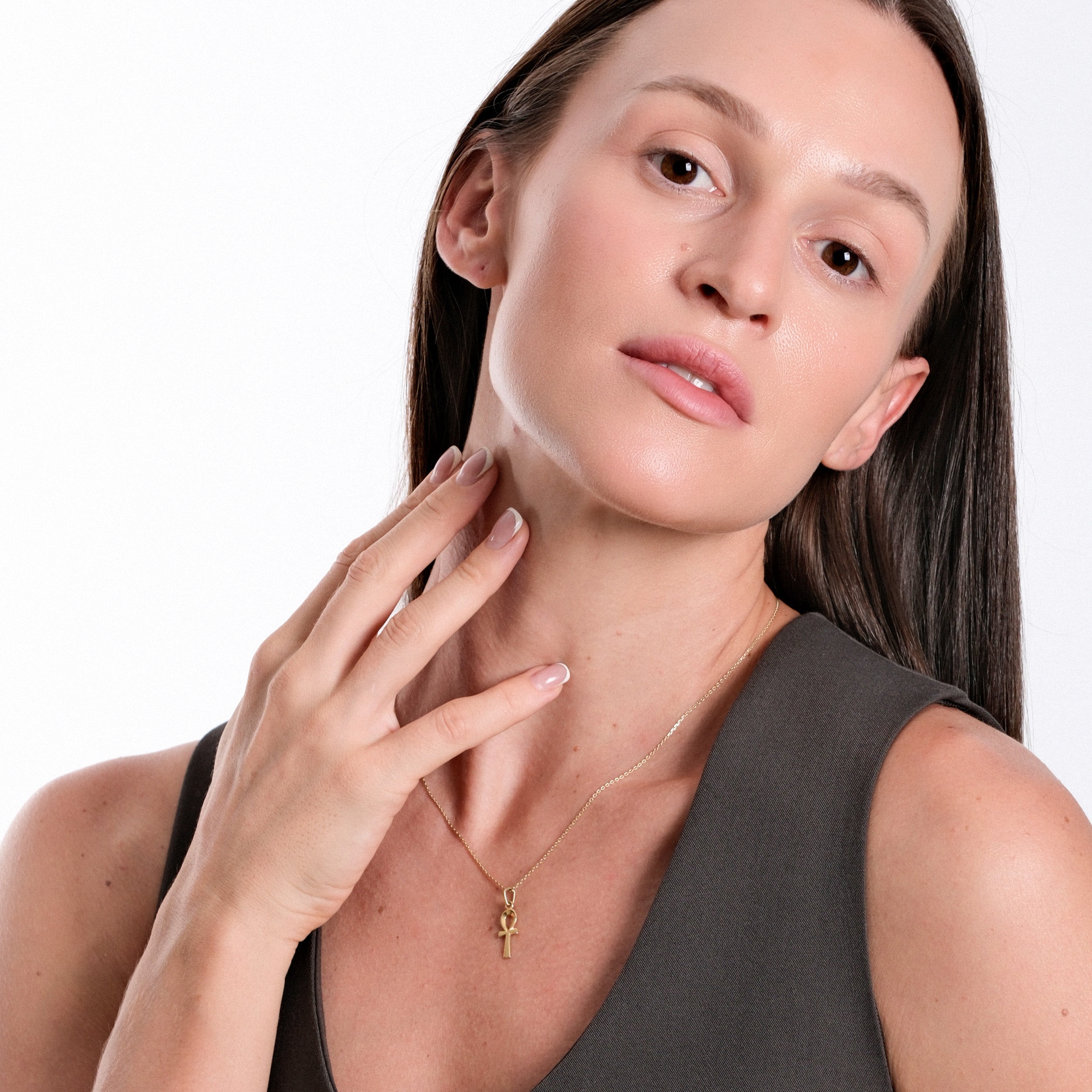 Woman with long hair wearing gold ankh necklace and gray top, showcasing elegant jewelry and fashion style.