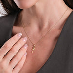 Woman wearing elegant gold ankh necklace, showcasing minimalist style and manicured nails on a dark blouse.