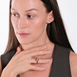 Woman wearing elegant gold necklace with ruby cross pendant, touching chest, showcasing jewelry fashion.