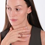 Woman wearing elegant gold necklace with ruby cross pendant, touching chest, showcasing jewelry fashion.