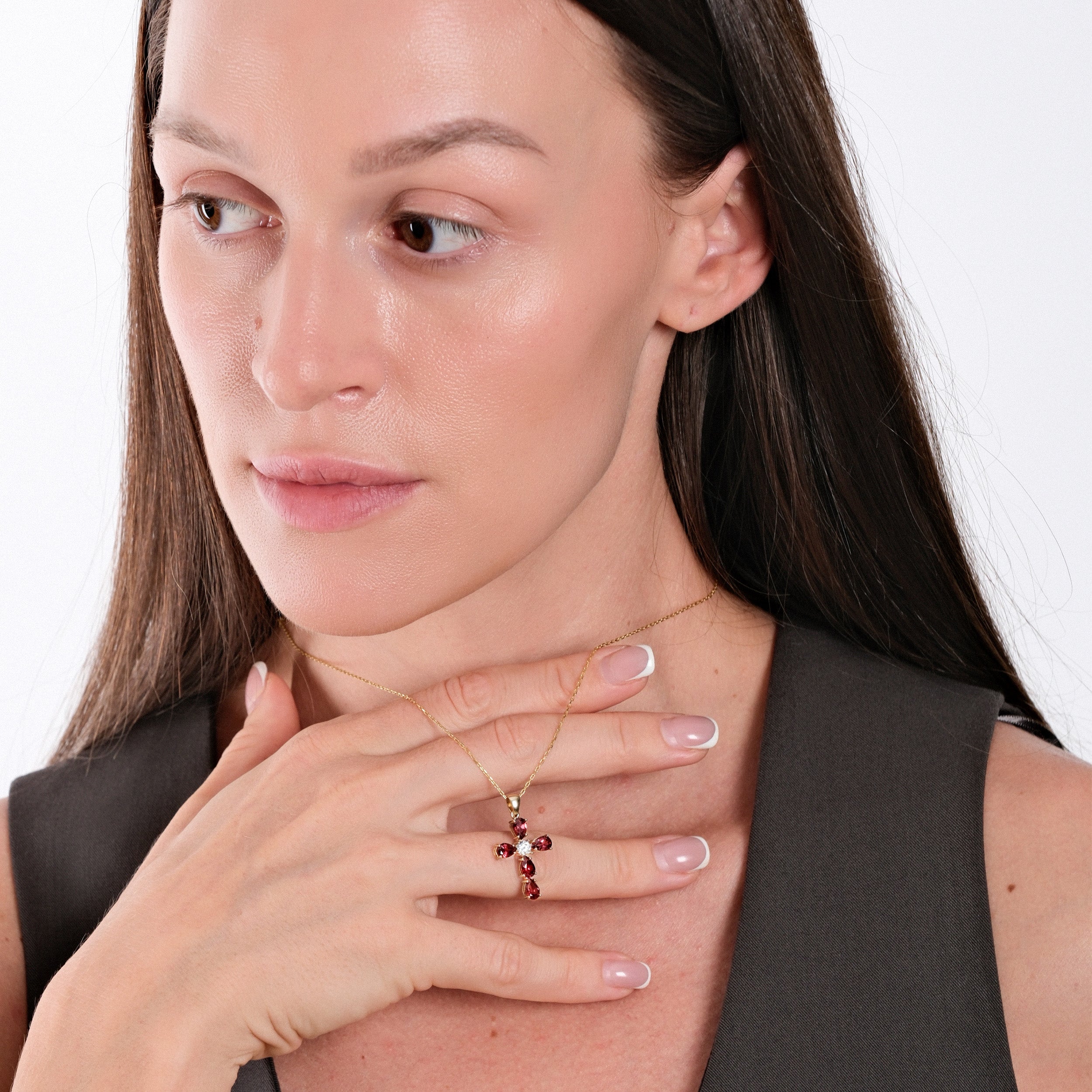 Woman wearing elegant gold necklace with ruby cross pendant, touching chest, showcasing jewelry fashion.