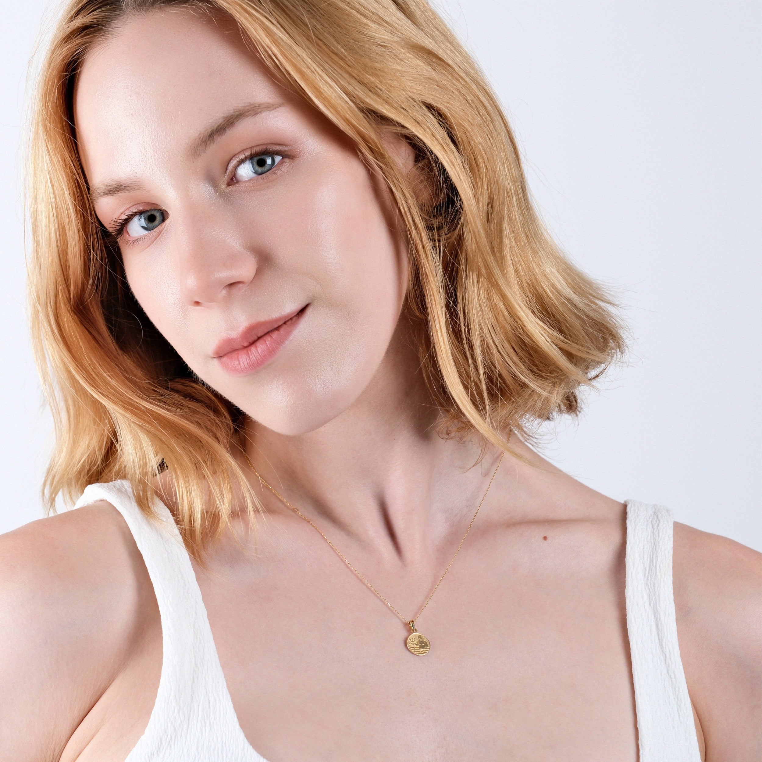 Smiling woman with blonde hair wearing a gold necklace and white top, exuding elegance and simplicity.