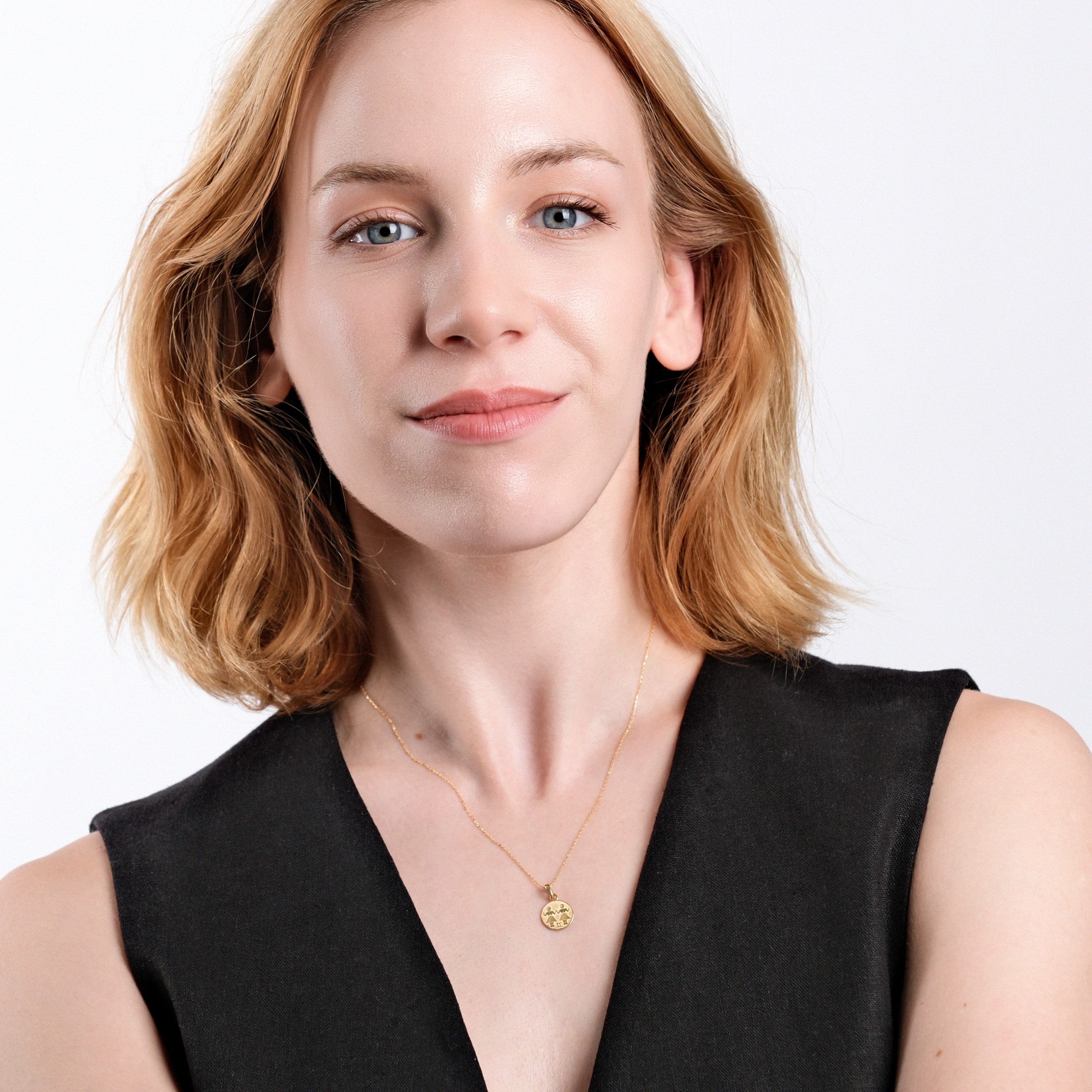 Woman with short blonde hair wearing black top and gold necklace, smiling confidently against white background.