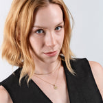 Woman with short blonde hair wearing a black top and gold necklaces, looking confidently at the camera.