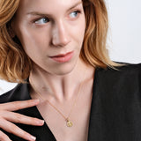 Woman wearing elegant gold necklace with pendant, black outfit, looking away, studio portrait.
