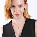 Smiling person wearing a black top and gold pendant necklace against a white background.