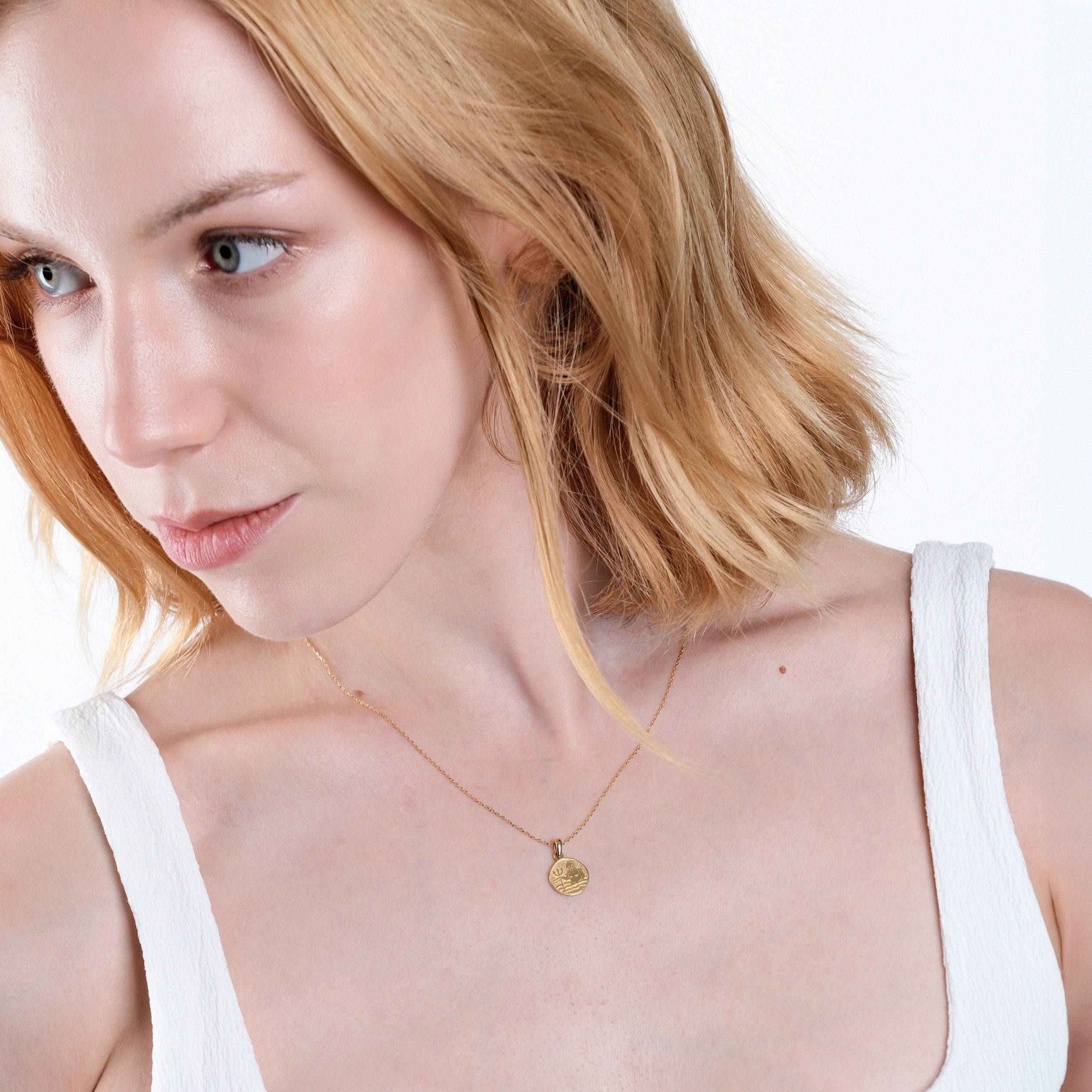 Blonde woman with short hair wearing a gold necklace and white top, looking thoughtfully to the side.