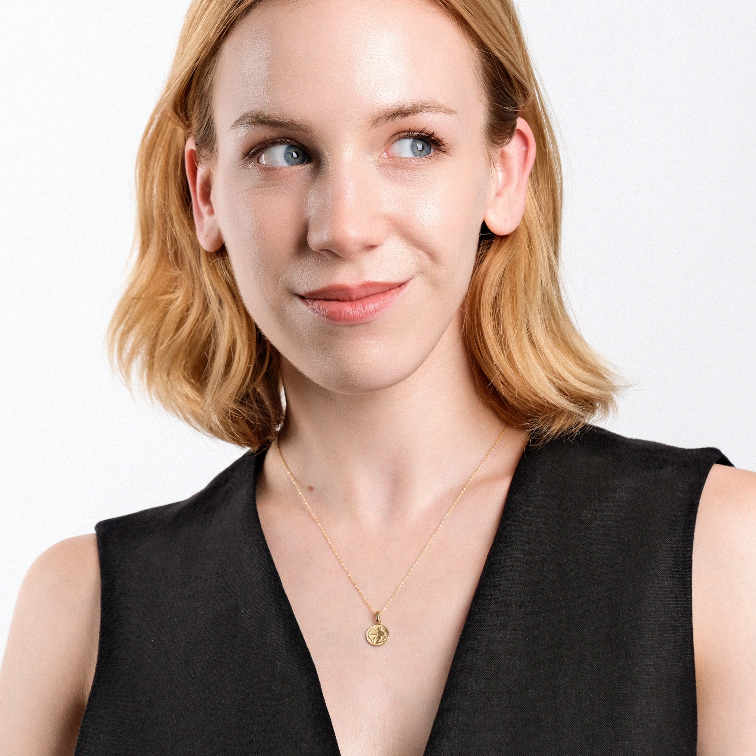 Woman with short blonde hair wearing a black top and gold pendant necklace, smiling confidently.