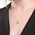 Elegant gold necklace with round pendant on woman wearing black top, showcasing minimalist jewelry style.