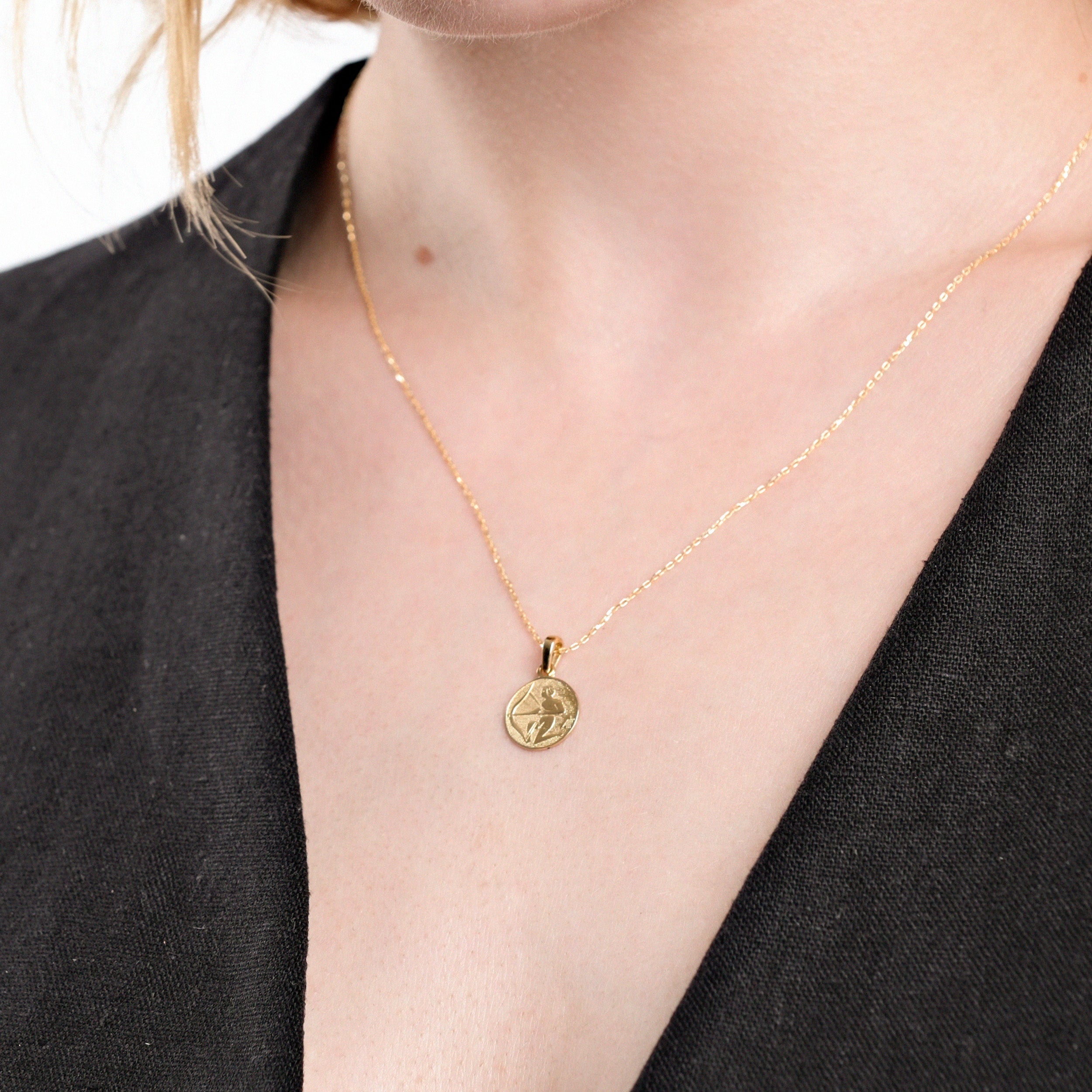Elegant gold necklace with round pendant on woman wearing black top, showcasing minimalist jewelry style.