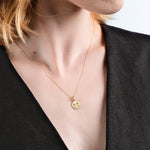 Woman wearing elegant gold pendant necklace on a delicate chain, paired with a stylish black top.