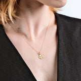 Woman wearing elegant gold pendant necklace on a delicate chain, paired with a stylish black top.