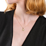 Woman wearing a gold clover pendant necklace, black dress, close-up on neck and jewelry.