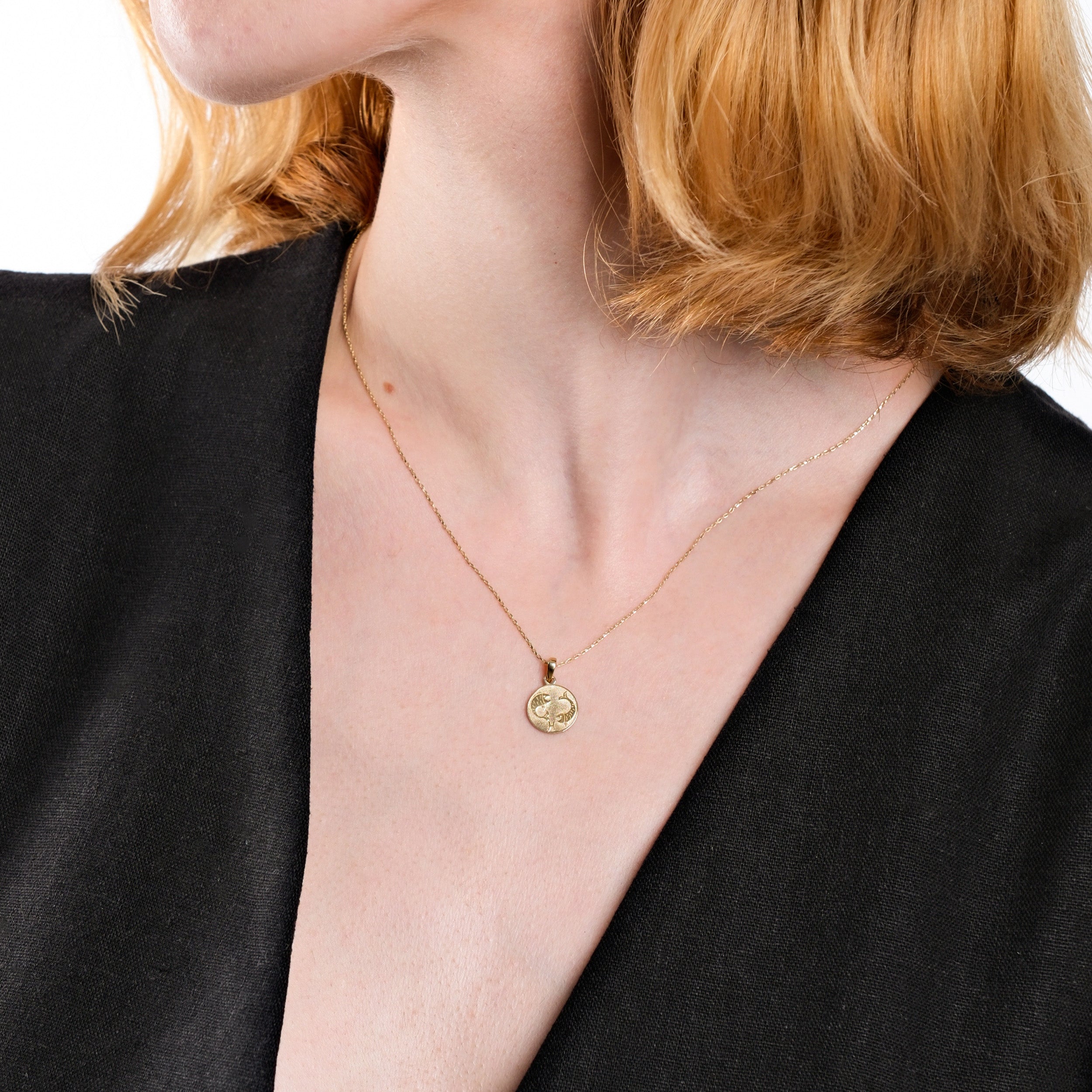 Woman wearing a gold clover pendant necklace, black dress, close-up on neck and jewelry.