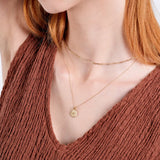 Woman wearing layered gold necklaces with a textured brown top, showcasing elegant minimalist jewelry style.