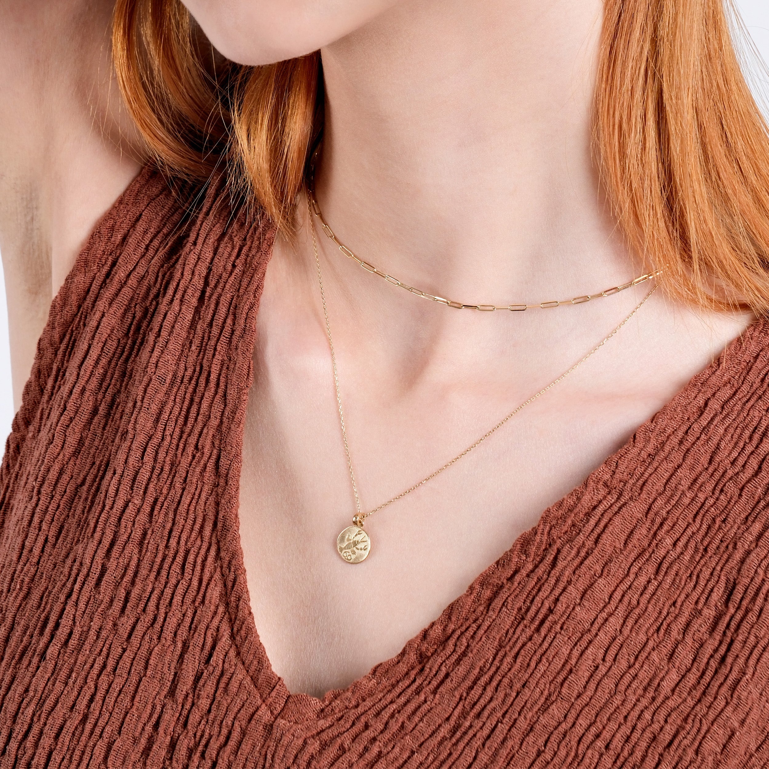 Woman wearing layered gold necklaces with a textured brown top, showcasing elegant minimalist jewelry style.