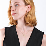 Woman with short blonde hair wearing black top and gold necklace, looking sideways on white background.