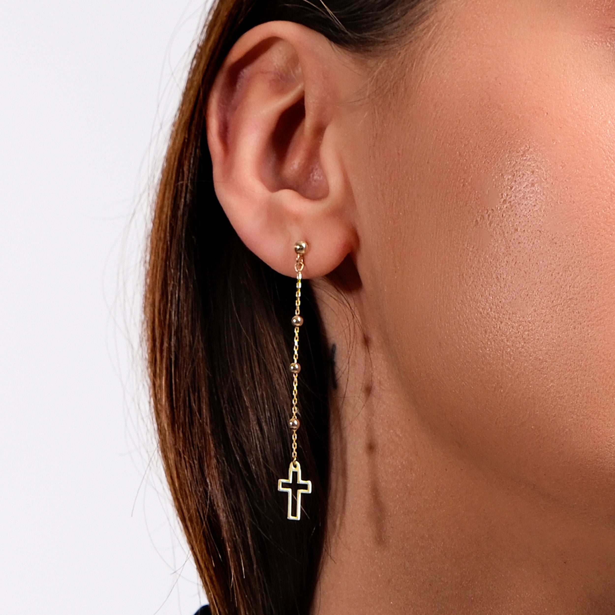 Close-up of woman's ear with elegant gold cross dangling earring, showcasing minimalist jewelry style.