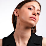 Close-up of a woman wearing cross earrings, black top, confident expression, on a white background.