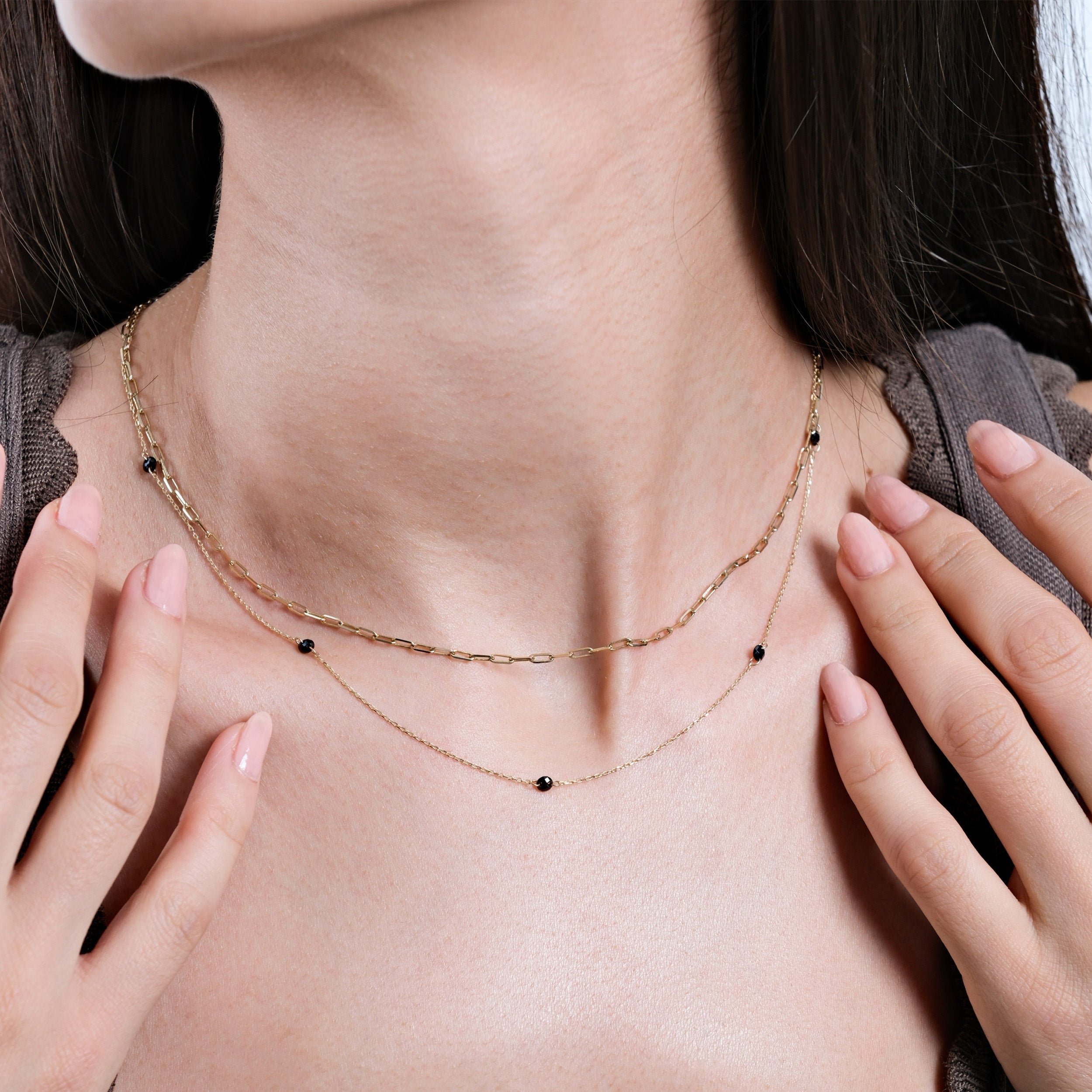 Woman wearing delicate layered gold necklaces with black bead accents, minimalistic fashion jewelry close-up.