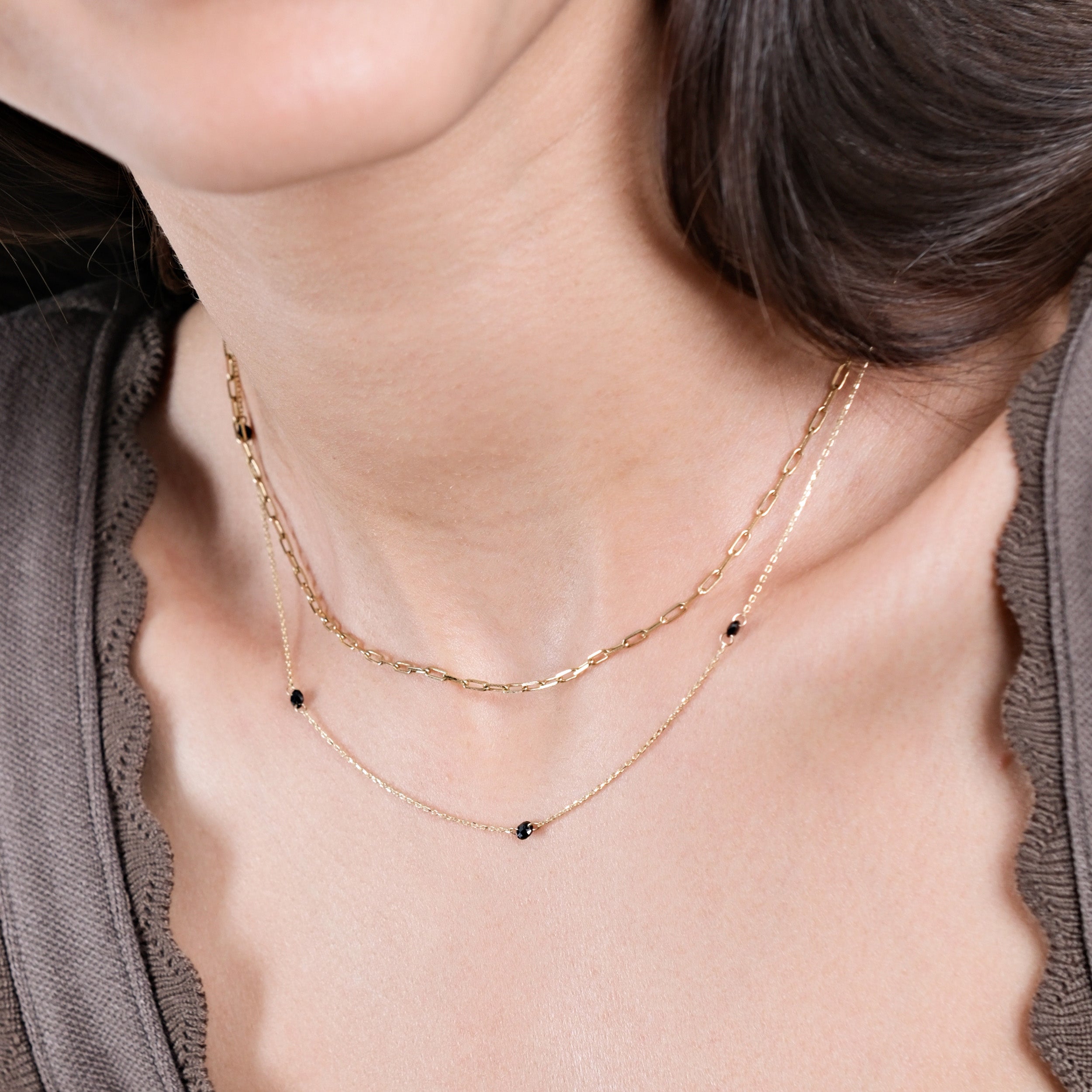 Woman wearing elegant layered gold chain necklaces with black beads, showcasing modern jewelry fashion.