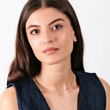 Young woman with long brown hair wearing a blue top and gold necklace, looking confidently at the camera.