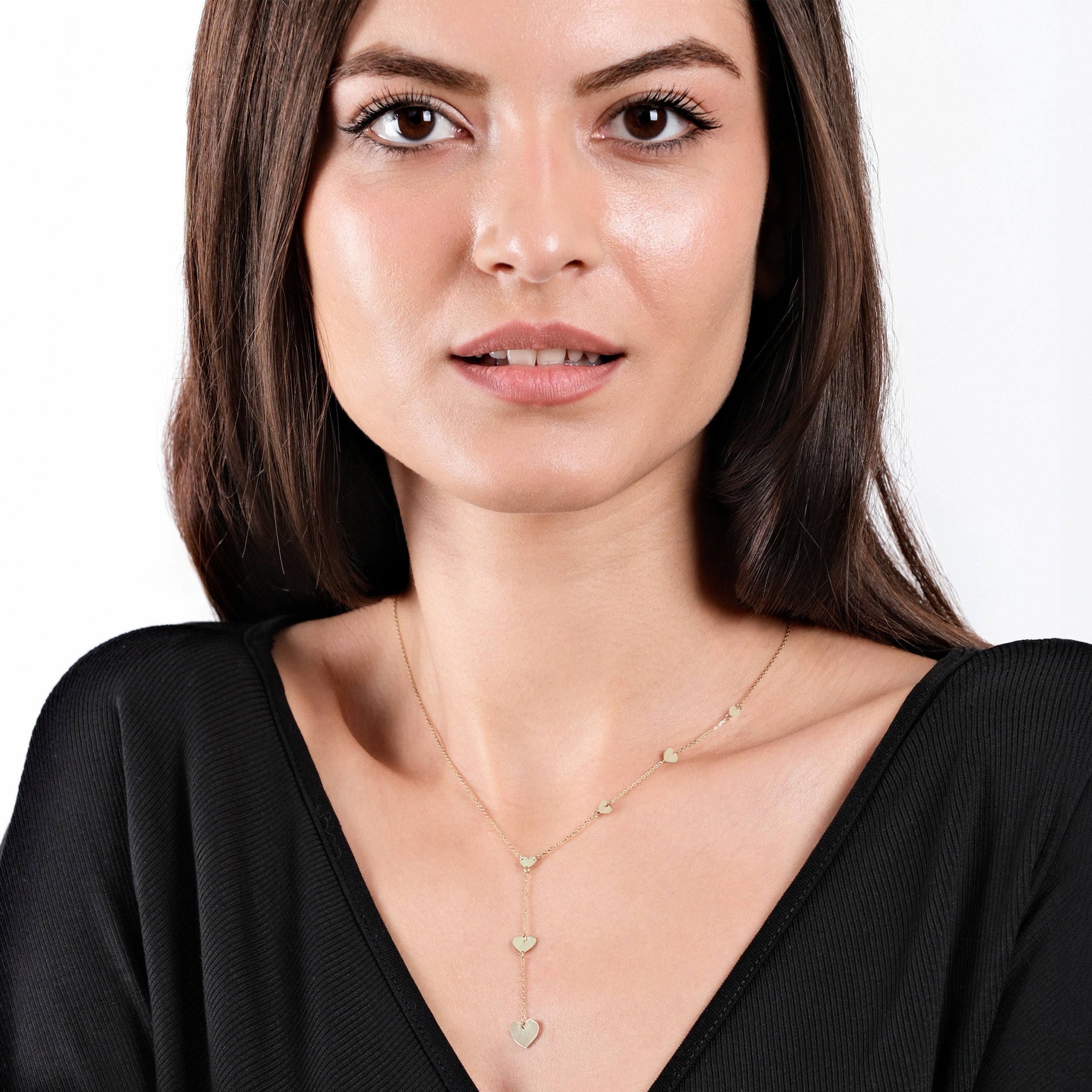 Woman wearing a black top and heart-shaped gold necklace, showcasing elegant jewelry style.