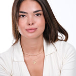 Woman in white top with layered gold necklaces, wearing minimal makeup, against a white background.
