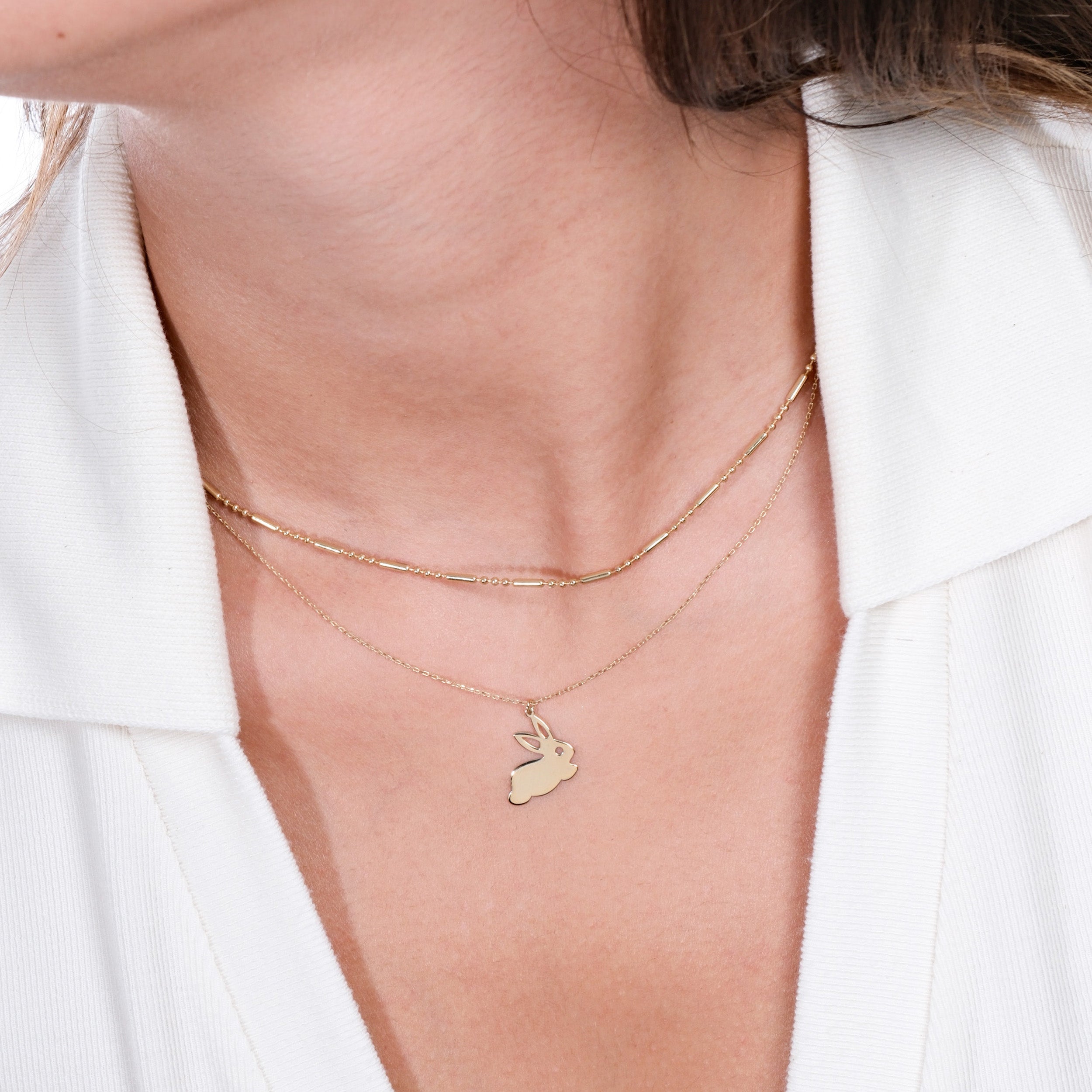 Woman wearing layered gold necklaces with a rabbit pendant, contrasting against a white collared shirt.