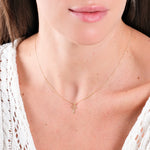 Woman wearing delicate gold cross necklace with white lace top, showcasing elegant minimalistic jewelry style.