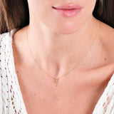 Woman wearing delicate gold cross necklace with white lace top, showcasing elegant minimalistic jewelry style.