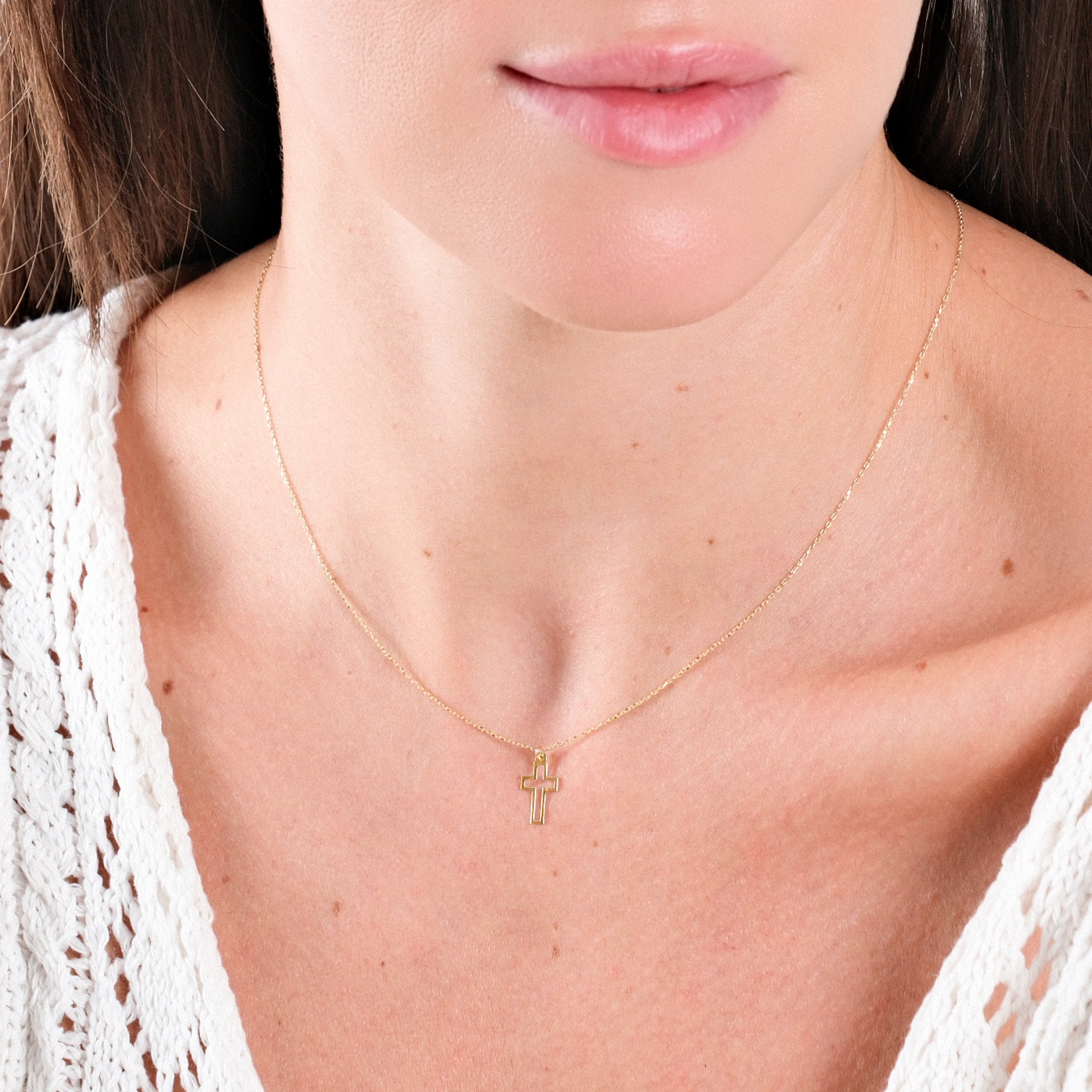Woman wearing delicate gold cross necklace with white lace top, showcasing elegant minimalistic jewelry style.