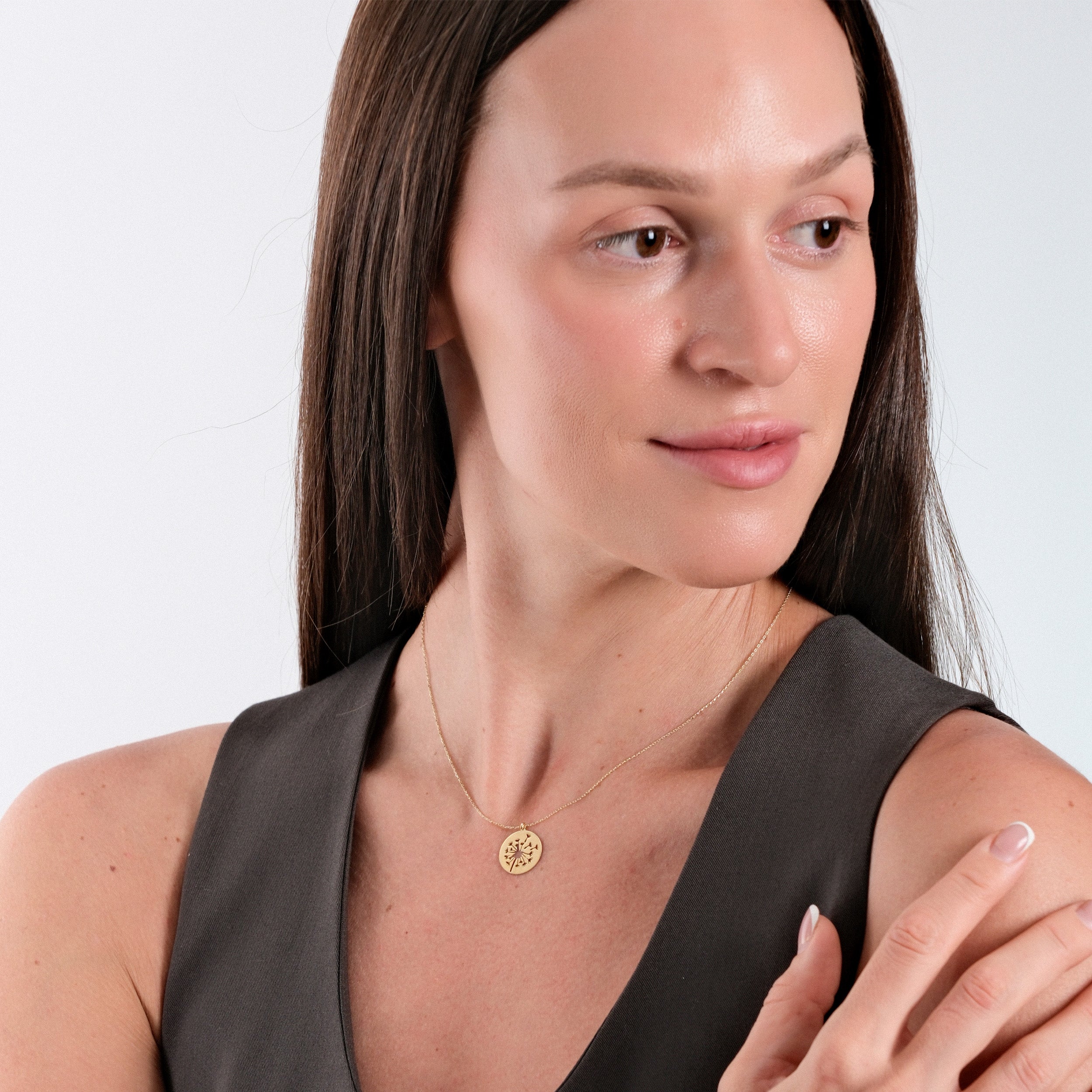 Woman wearing elegant gold necklace with pendant, dressed in gray top, showcasing minimalist fashion style.
