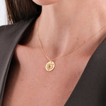 Gold necklace with floral pendant on woman wearing a dark blouse, elegant jewelry close-up.