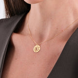 Gold necklace with floral pendant on woman wearing a dark blouse, elegant jewelry close-up.