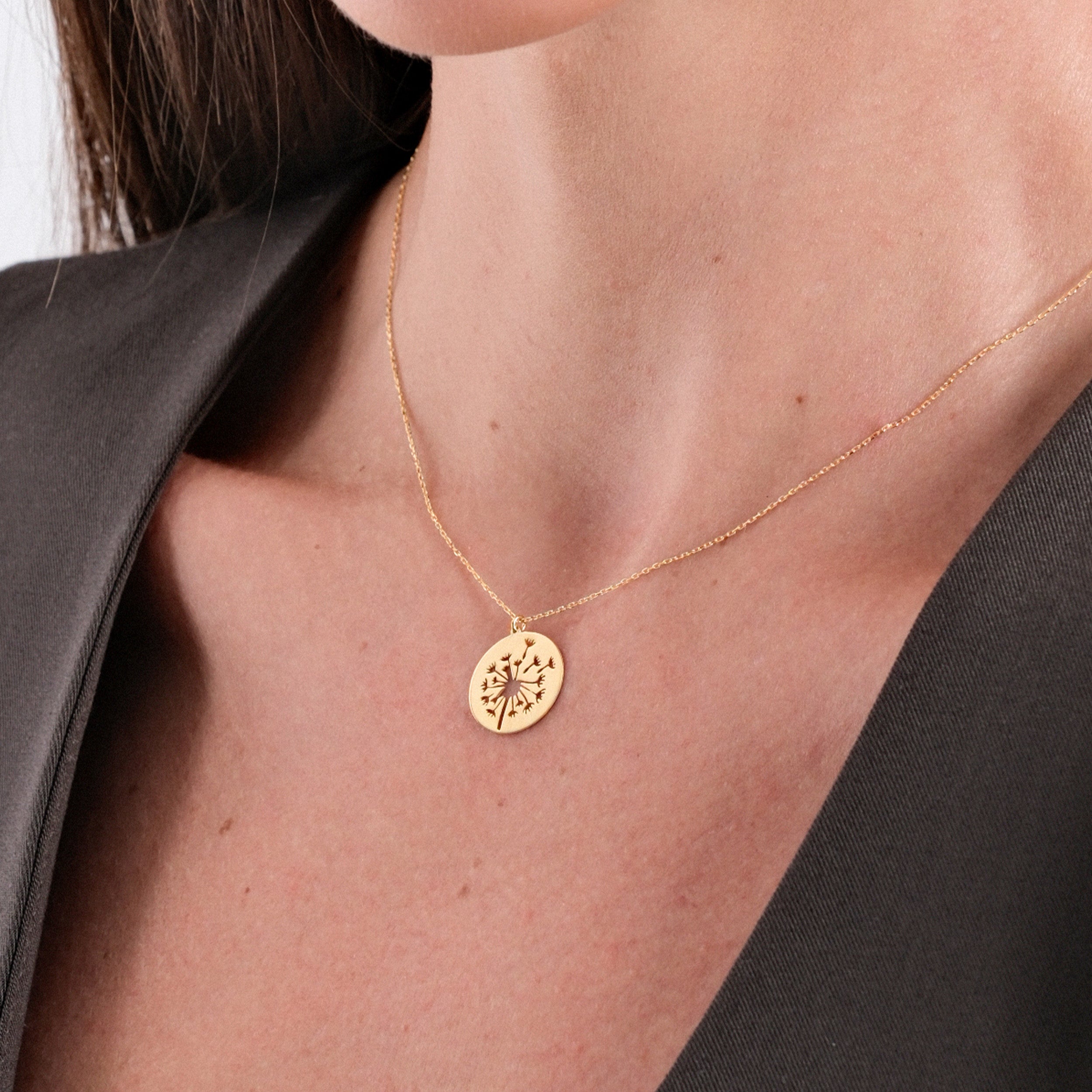 Gold necklace with floral pendant on woman wearing a dark blouse, elegant jewelry close-up.