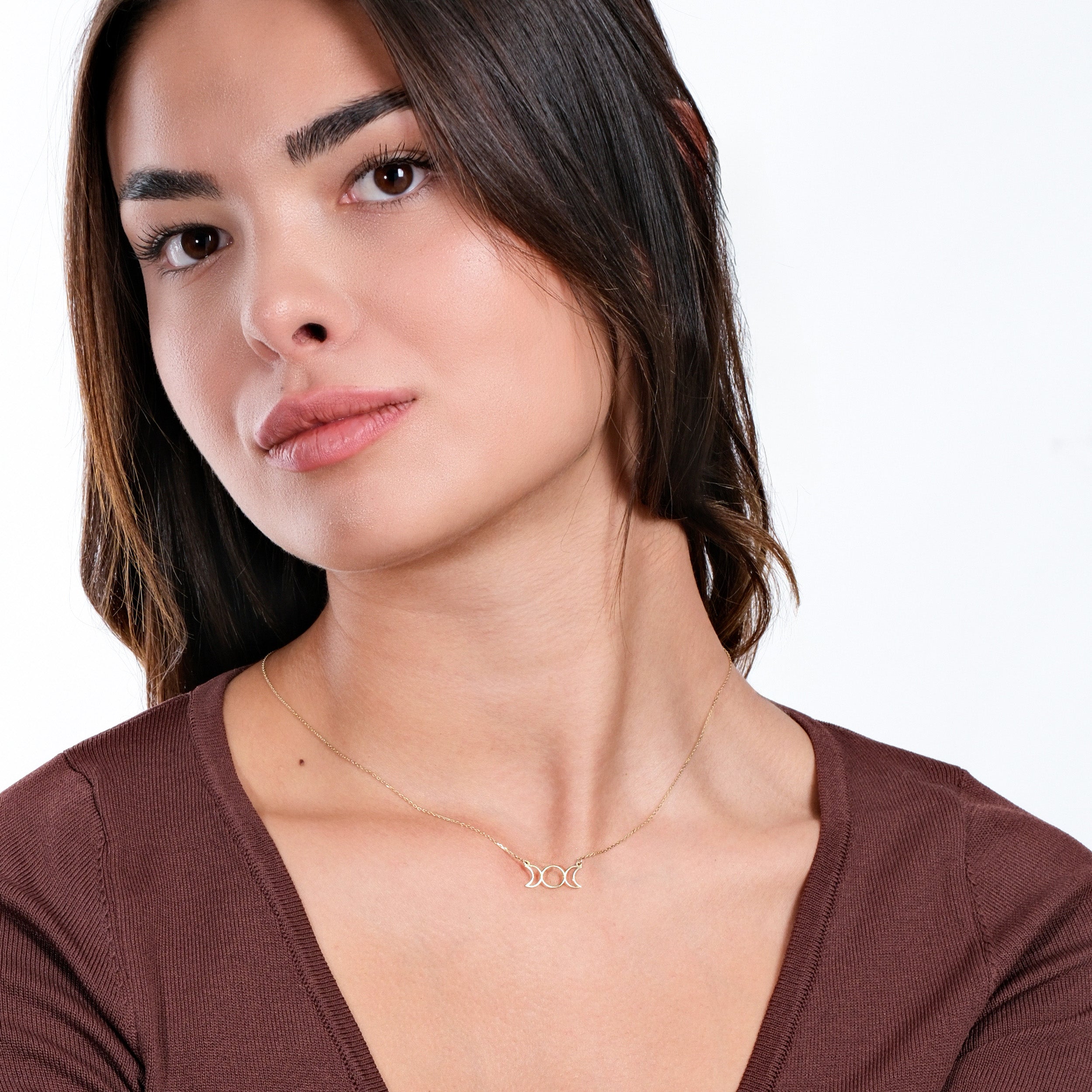 Woman wearing elegant gold necklace with crescent moon design on a brown top, posing against white background.