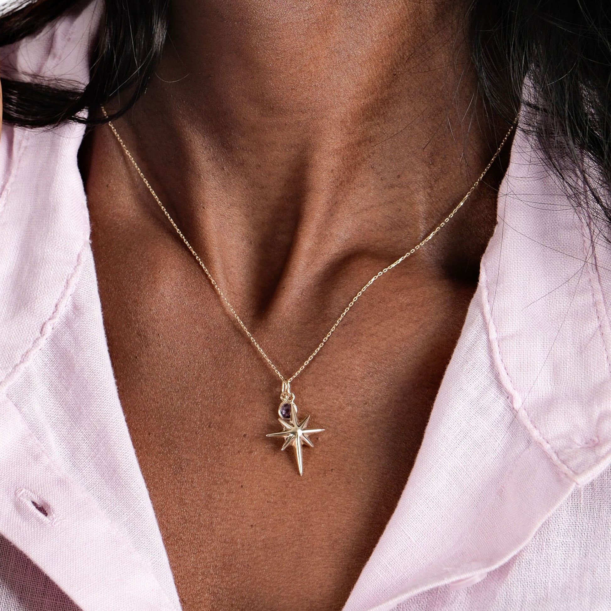 Gold star pendant necklace on woman's neck, pink shirt background, elegant jewelry fashion.