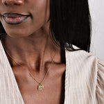 Woman wearing a gold necklace with initial pendant, dressed in a beige striped blouse.