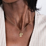 Gold necklace with letter "E" pendant on woman's neck, wearing a striped shirt. Elegant personalized jewelry.