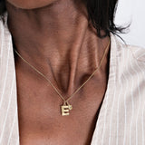 Gold necklace with letter "E" pendant on woman's neck, wearing a striped shirt. Elegant personalized jewelry.